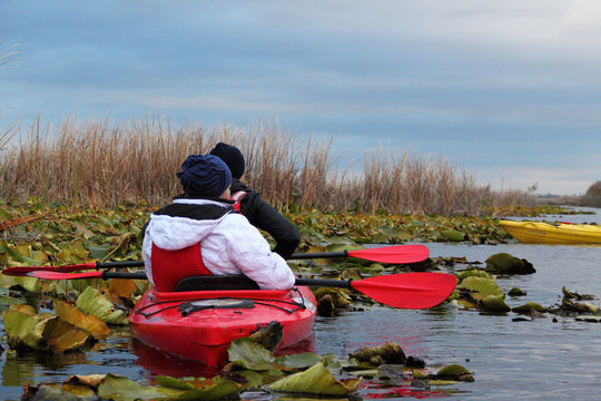 Two girls in a red kayak-deuce lilies and leaves on a cloudy autumn day in the autumn lake