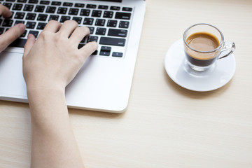 Woman's hands typing on laptop keyboard with a cup of coffee on wooden desk.