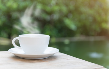 Cup of coffee on wood table with green pond background