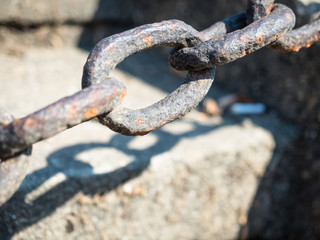 Picture of the selective focus on a rusty iron chain against the blurred background of the gray stones. Rusty iron chain close up.