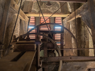 Picture of the rusty mechanism in the wooden belfry of the church. The wall of the belfry made of...