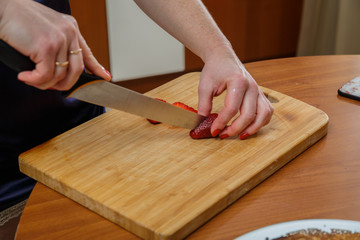 Beautiful female hands cut strawberries in the kitchen