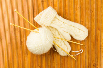 roll of white soft knitting yarn and knitting mittens