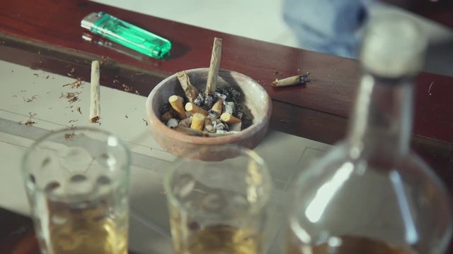 Substance abuse, drugs and narcotics. Liquor bottle and glasses, ashtray with cigarette butts, hashish joints on table at home