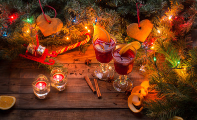 Fototapeta na wymiar Two glasses of mulled wine with orange slices, candles and Christmas tree with garland and toys