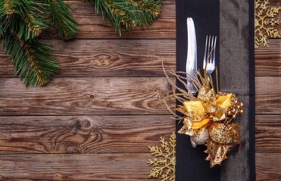 Christmas table place setting decorated black napkin with fork and knife, gold flower and snowflakes and christmas pine branches.