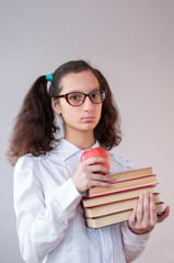 Schoolgirl with glasses holding a stack of books and red apple