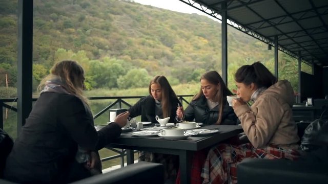 Young cheerful women eating in a restaurant on a terrace near the pond