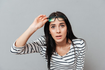 Young woman wearing eyeglasses shocked over grey background