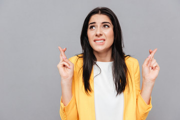 Confused young woman crossed fingers over grey background