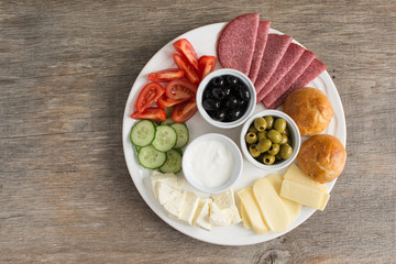 Traditional Turkish breakfast platter on the grey wooden table, top view: pogaca pasties, vegetables, cheeses, olives and halal turkey salami, selective focus; copy space for text