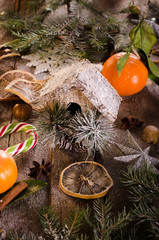 Magic Christmas background - vintage wood, candy cane, house, cinnamon, star anise, sweet mandarins with green leaves, cones, snowflakes. New Year. Top view, blank space