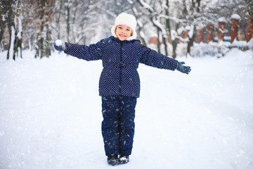 Small girl playing with snow in a park. The concept of childhood and the winter season.