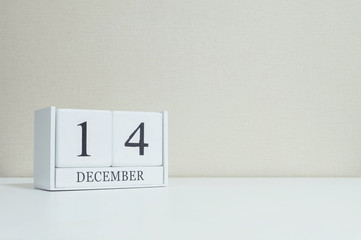 Closeup white wooden calendar with black 14 december word on blurred white wood desk and cream color wallpaper in room textured background with copy space , selective focus at the calendar