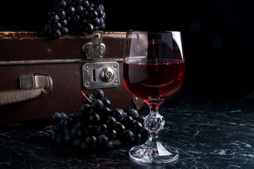 Glass of red wine on dark marble background. Cluster of blue gra