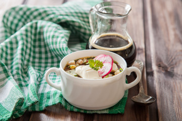 Popular spring cold soup okroshka with kvass. Okroshka in a bowl,  kvass in a jug,  on wooden table. Selective focus