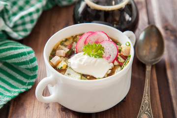 Popular spring cold soup okroshka with kvass. Okroshka in a bowl,  kvass in a jug,  on wooden...