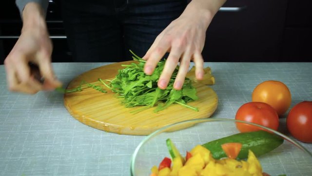 Girl cook slices arugula on a wooden board in kitchen