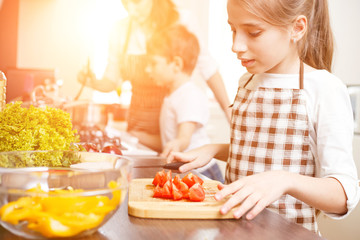 Young teenage girl cooking together with her family in the kitchen. Cute girl chopping tomatoes for salad