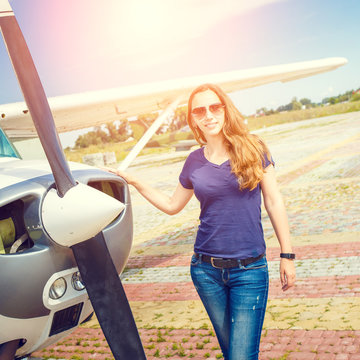 Young smiling woman standing near private plane ready for flight. Warm color toned image. Aviation school background