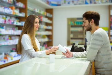 Obraz premium Attractive smiling pharmacist giving her client pills at the local pharmacy