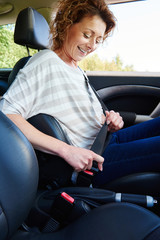 Smiling woman with curly hair buckling seat belt in car