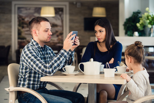 Modern family values. Father addicted about using electronic devices tablet pc, while his wife and daughter unhappy sitting in a cafe