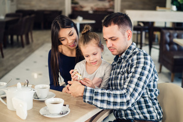 family, parenthood, technology people concept - happy mother, father and little girl having dinner taking selfie by smartphone at restaurant