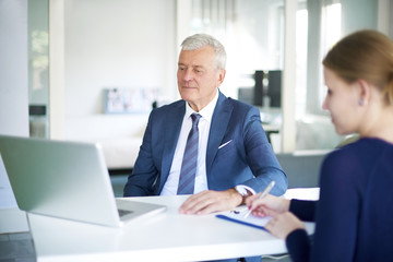 Business meeting. Shot of a senior executive financial businessman sitting in front of laptop and consulting with his young assistant in the office.