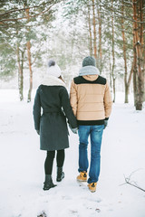 Young couple walking in a snowy winter forest in their warm winter clothes