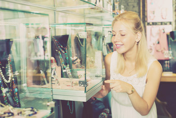 Fototapeta na wymiar Female choosing bijouterie in glass showcase in boutique