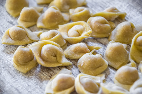  Raw italian cappelletti, fresh homemade pasta stuffed with cheese and meat on rustic wood table. Natural light.