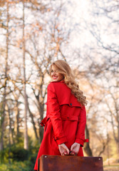 Back view of a beautiful young woman with vintage suitcase in a autumn park. She is looking at camera.