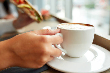 woman drinking coffee and eating sandwich at cafe
