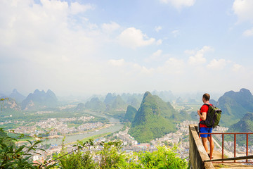 Fototapeta na wymiar Hiker with backpack enjoying view from top of the hill with beautiful view on Yangshuo city with mountains around. Yangshuo, China.