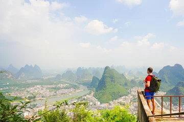 Fotobehang Hiker with backpack enjoying view from top of the hill with beautiful view on Yangshuo city with mountains around. Yangshuo, China. © upslim