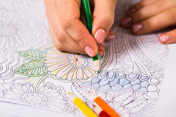 Girl paints a coloring book for adults with crayons