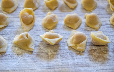  Raw italian cappelletti, fresh homemade pasta stuffed with cheese and meat on rustic wood table. Natural light.