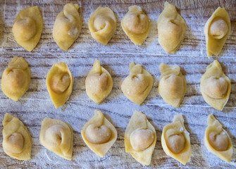  Raw italian cappelletti, fresh homemade pasta stuffed with cheese and meat on rustic wood table. Natural light.