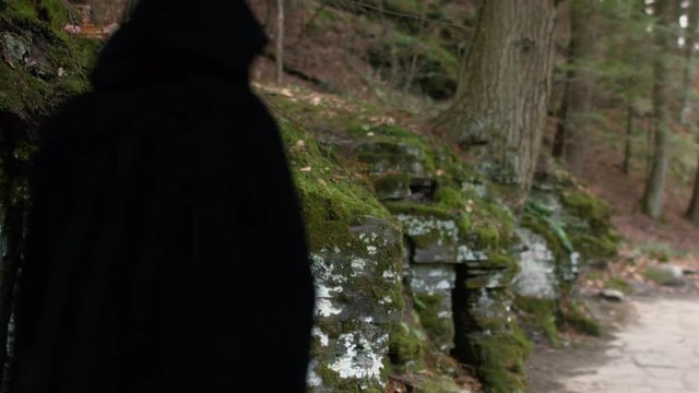 Cloaked Figure Walks Down Mossy Stone Path In The Woods