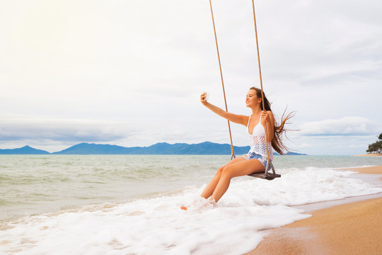 Young smiling woman on beach swing making selfie.  Vacation concept.