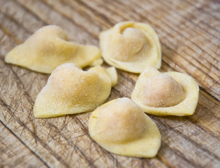  Raw italian cappelletti, fresh homemade pasta stuffed with cheese and meat on rustic wood table. Natural light.