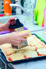 Woman hands grating cheese on the pizza. Young woman preparing the pizza in the kitchen.