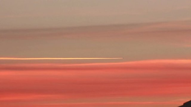 Airplane flying across the frame leaving contrail on an orange sky