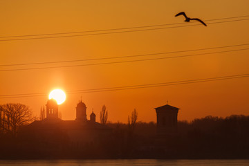 Beautiful sunrise over a church with trees around and birds flyi