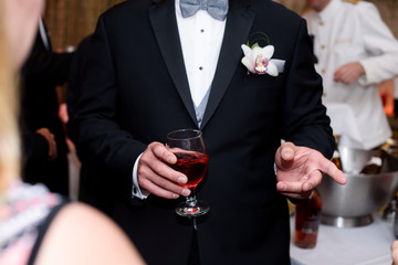 Man in black tuxedo holds glass of red wine