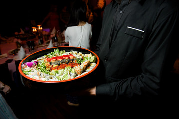 Waiter in black carries large dish with sushi