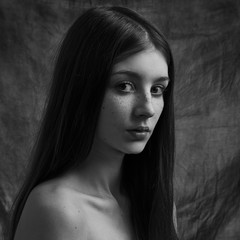 Dramatic black and white portrait of a beautiful lonely girl with freckles isolated on a dark background in studio shot