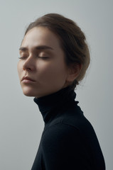 Dramatic portrait of a young beautiful girl with freckles in a black turtleneck on white background in studio - 129438648