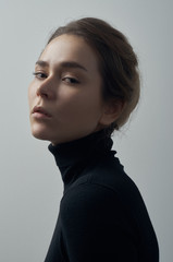 Dramatic portrait of a young beautiful girl with freckles in a black turtleneck on white background...